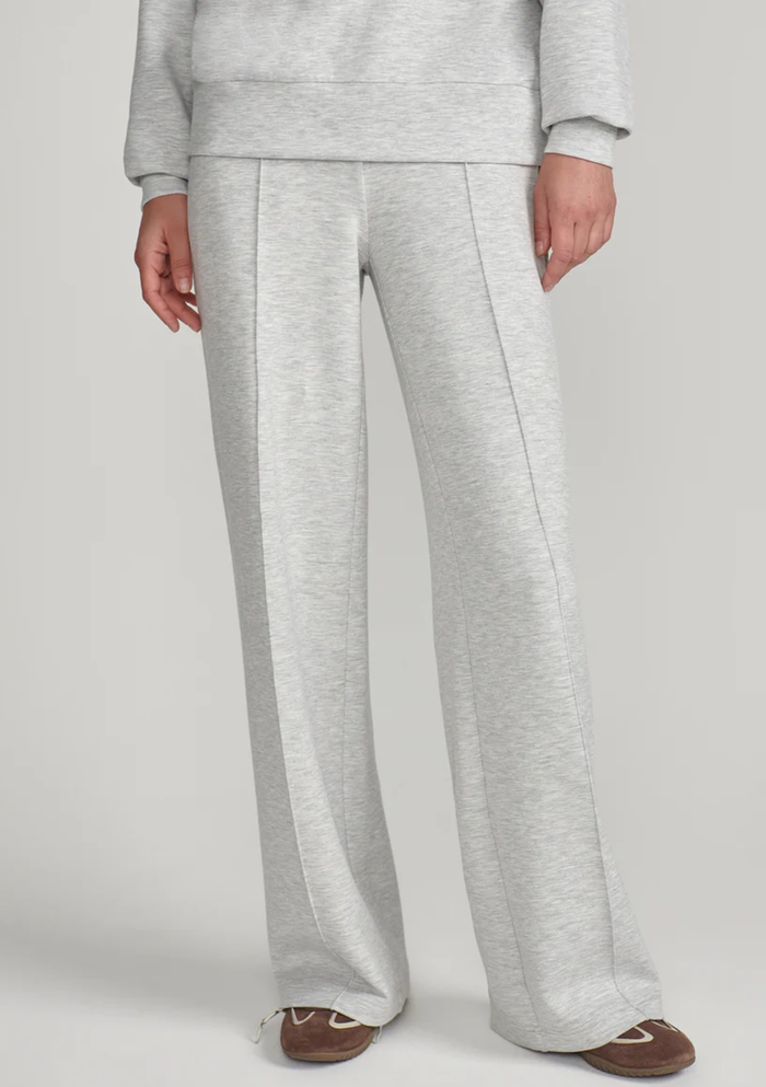 A person wearing light heather gray wide-leg sweatpants with a matching sweatshirt partially visible, standing against a plain light gray studio background.