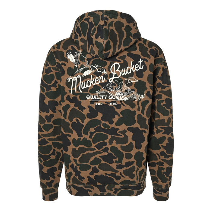 The Youth Wood Ducks Premium Duck Camo Hoodie by Mucker Bucket features a relaxed fit camo design with crossed duck calls, "Mucker Bucket," and "Quality Goods TRD MRK" in white on the back—perfect for young hunters.